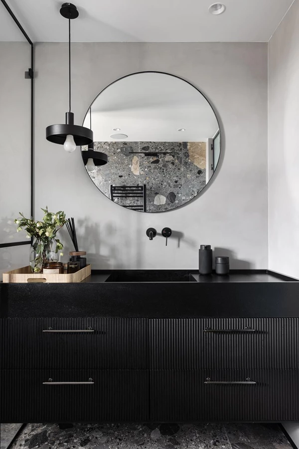 חדר הרחצה עוצב בגוונים כהים ודרמטיים ובו יחידת נגרות מחופה אצבעות עץ ומעליה שיש שחור