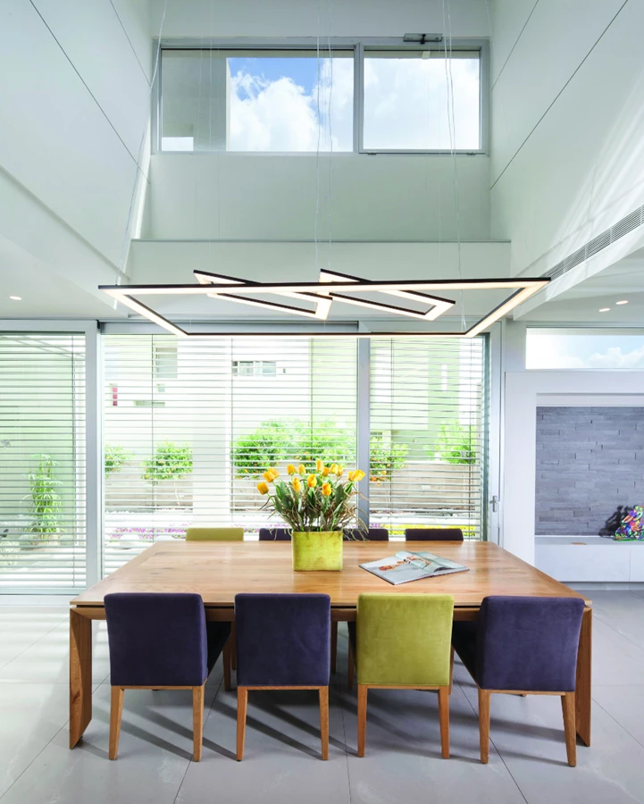 פינת האוכל שבאזור החלל הכפול: אוורירית ומוארת. גופי תאורה המשתלשלים מטה מרום התקרה  מוסיפים לה נופך אינטימי- חמים ועיצובם המלבני מעניק הד צורני לשולחן.