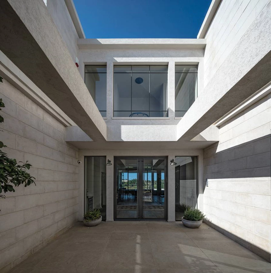 חלל ביניים פתוח לשמיים, שנחשף עם פתיחת דלת העץ האטומה שבחזית ובסופו מתגלה הכניסה הרשמית השקופה.