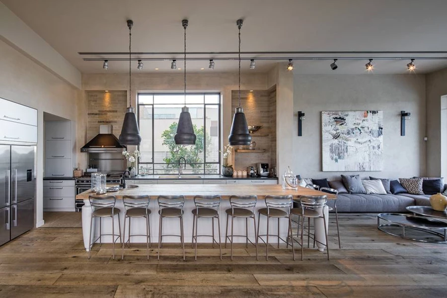 המטבח: חזיתות בגימור שלייף לק מט, משטח כיור שחור המדמה אבן בזלת, חיפוי בריקים בגומחות שמשני עבריו, יחידת אי גדולה שעיצובה מהדהד זיקה למראה קלאסי, ושלושה גופי תאורה גדולים ושחורים שמשתלשלים מעליה. לצד האי נראית פינת המשפחה. נגרות מטבח: