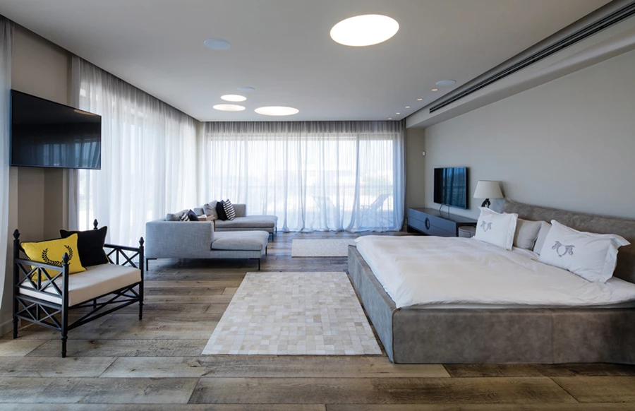 חדר השינה רחב הידיים כחלל מסוגנן ומוקפד מוקף מרפסת דק גדולה המעניקה תצפית אל הנוף.