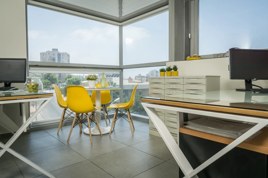 שולחנות עם רגלי איקס ממתכת בלבן ופלטות עץ לבנות משולבות בעץ אלון לצד כסאות אירוח איימס צהובים