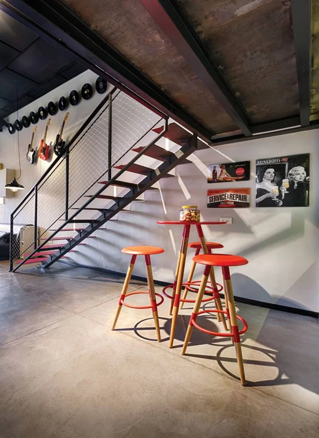 בניחוח המוסיקה של שעות הערב: גיטרות ישנות ששוקמו ותקליטים של פעם מעטרים את הקיר. מתחת לגרם המדרגות: שולחן וכיסאות בר בגון אדום שנגזר מצבעי הלוגו, בדומה לגונן של המדרגות.