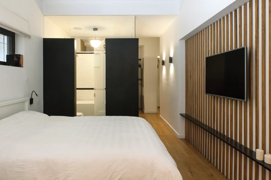 חדר השינה וחדר הרחצה הצמוד אליו ומצויד בדלת זכוכית עם טקסטורה מודפסת בצפיפות משתנה. חיפוי קיר בסרגלי עץ אופקיים מוסיף עניין ומגלם המשכיות עיצובית.