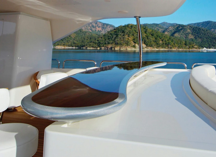 שולחן בר על הסיפון: משטח מרחף בקו מתעגל דמוי ירח משהו. שילוב של עץ טיק בציפוי אפוקסי מבריק עמיד במיוחד בפני קרינת UV ותנאי סביבה ימית עם גימור היקפי של אריג טקסיליום.