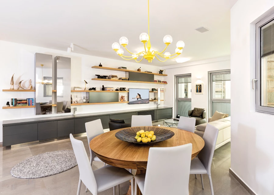 פינת האוכל במרכז החלל הציבורי מקבלת את פני הנכנסים. מעליה: גוף תאורה דקורטיבי שנרכש בשוק הפשפשים, נצבע בצהוב עז כנגיעה של צבע במארג הגוונים המאופק, ולצד השולחן העגול שטיח בעיצוב תואם. שולחן אוכל: