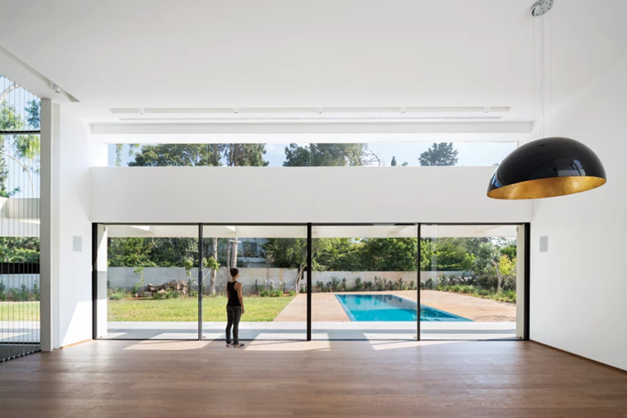 ביציאה מהחלל הציבורי: ויטרינות במסגרות אלומיניום שחורות ומעודנות וחלון סרט מעליהן פותחים את החלל אל הגינה האחורית ומדגישים את החשיבות שניתנה לאור.