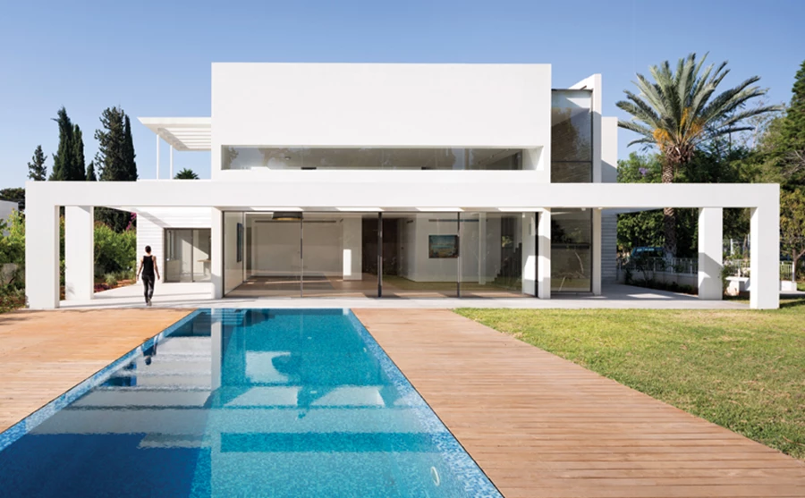 הגן שביציאה מחלל המגורים: שילוב של בריכת תעלות גלישה, דק ורחבות מרוצפות מתחת לפרגולה. ריצופן הזהה לריצוף הפנים מייצר רצף ישיר בין שני המרחבים.