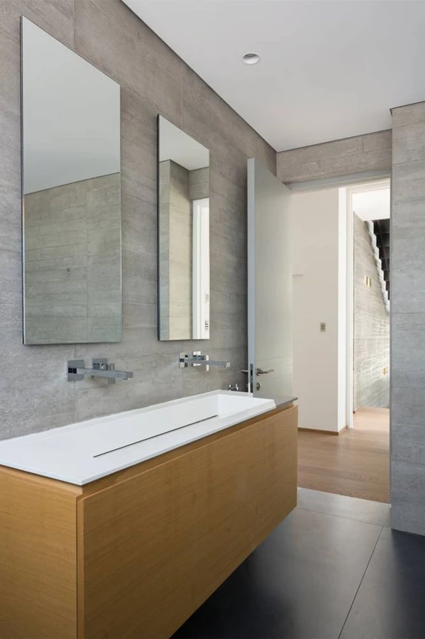 עיצוב תמציתי ומדויק גם בחדרי הרחצה בקומה העליונה: חיפוי באריחים במראה בטון, גווני לבן ונגרות עץ בהירה בקווים נקיים.