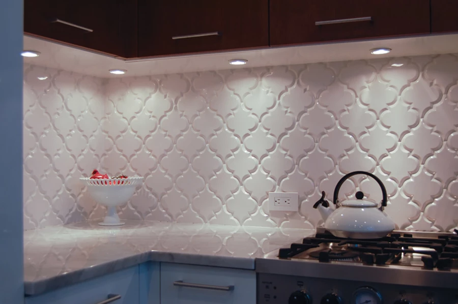 המטבח שסופח לחלל הציבורי: יחידת כיור מחופת שיש קררה שצדה הפונה לסלון משמש כדלפק אכילה, ארונות לבנים, ואריחי חיפוי בתצורת טיפות מרוקניות עם מעין מסגרת פזה.