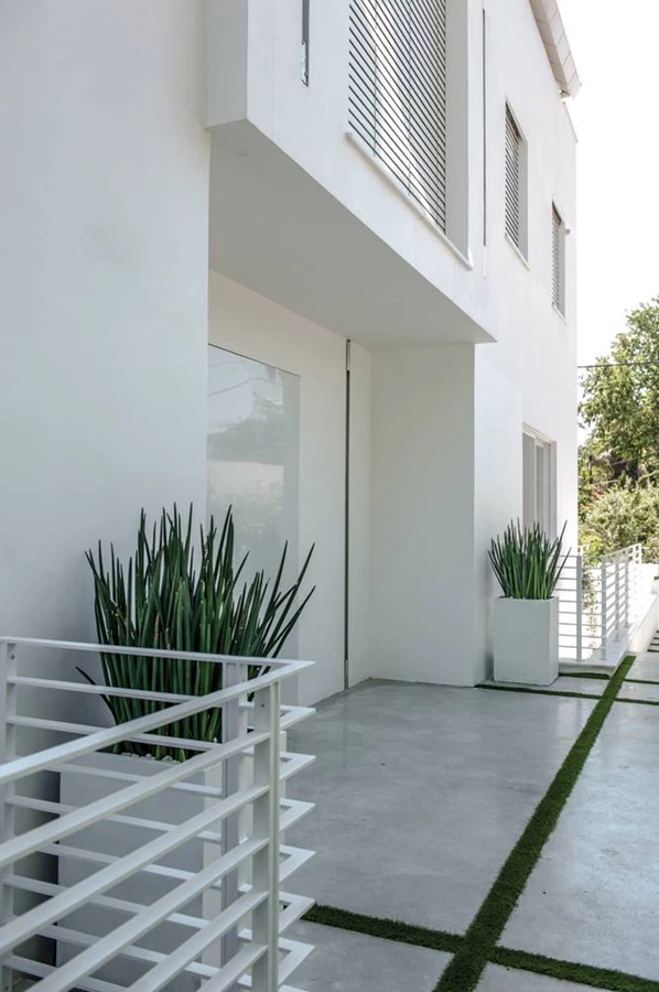 מבואת הכניסה שבצד הבית: דלת בגימור צבע לבן מבריק נפתחת ב-90 מעלות, וחושפת את הפטיו שבמרכז החלל.