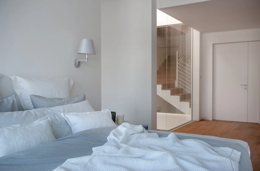 סוויטת השינה הממוקמת מעברו האחד של מעבר רחב בקומה הראשונה. פתח שקוף גדול חושף את הפאטיו המלווה את קומות המבנה, ומרפסת חזיתית צופה אל הגינה והבריכה. ריצוף פרקט ועיצוב נקי שנצמד לגוני האפור והלבן של הבית. פרקט: