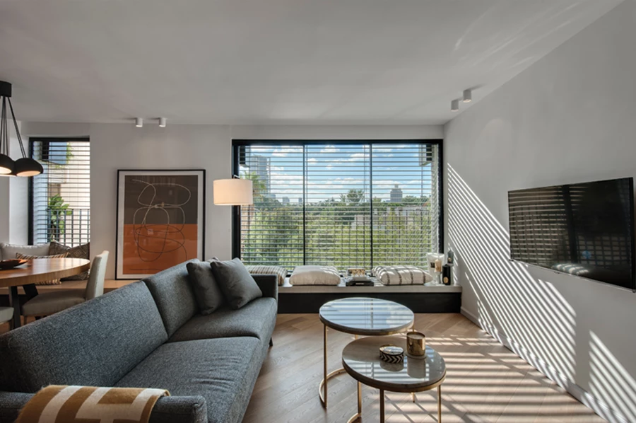 אזורי הסלון ופינת האוכל: עיצוב א-פורמאלי גמיש, המשמר מראה אותנטי וחם. הויטרינות נתונות בפרופיל אלומיניום שחור ודקיק דקיק החובר בחזותו לספסל שבתחתיתן, ומרבית פריטי הריהוט עוצבו ייעודית עבורו תוך שימוש בחומרים טבעיים והקפדה על שפה אסתטית המשלבת צורניות גראפית-גיאומטרית ומוטיב מעוגל. ויטרינות: כוכב אלומיניום, פריטי ריהוט: LEELOU HOME טולמנ