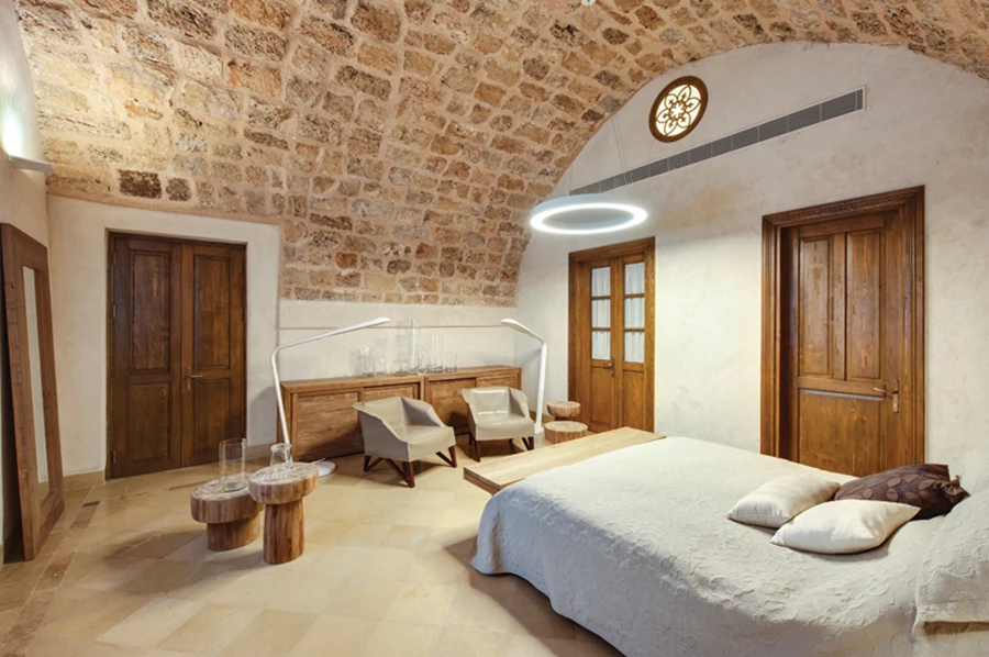 אחד מחדרי השינה: תקרת כורכר מקומרת, ריצוף באבן ביר זית בעיבוד טלטיש ידני, ונוכחות חמימה שנוסכים פריטי ריהוט מעץ בעיצוב המשמר פשטות אנינה.