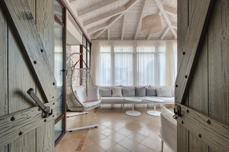 ביציאה מחדר שינה: סוג של מבנה גזיבו פינתי כחלופה למרפסת. תקרת עץ משופעת ופריטי ריהוט חוץ מסוגננים.