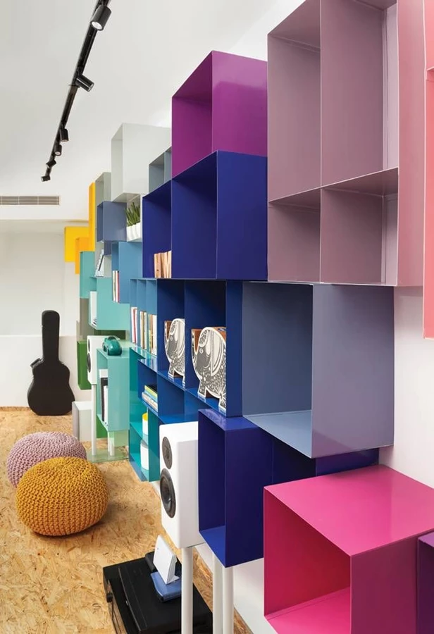 הספרייה שעוצבה ייעודית לחלל הציבורי: קומפוזיציה ססגונית של קוביות ברזל דק מאד בגדלים, עומקים וצבעים שונים. מתחת לספרייה: במה נמוכה מרחפת עשויה OSB עם תאורה סמויה שמופצת מתחתיה מגדירה את אזור המדיה ומשמשת גם לישיבה. פינת הישיבה שמולה מאזנת את המופע הצבעוני בגווניה הבהירים. ביצוע הספרייה: