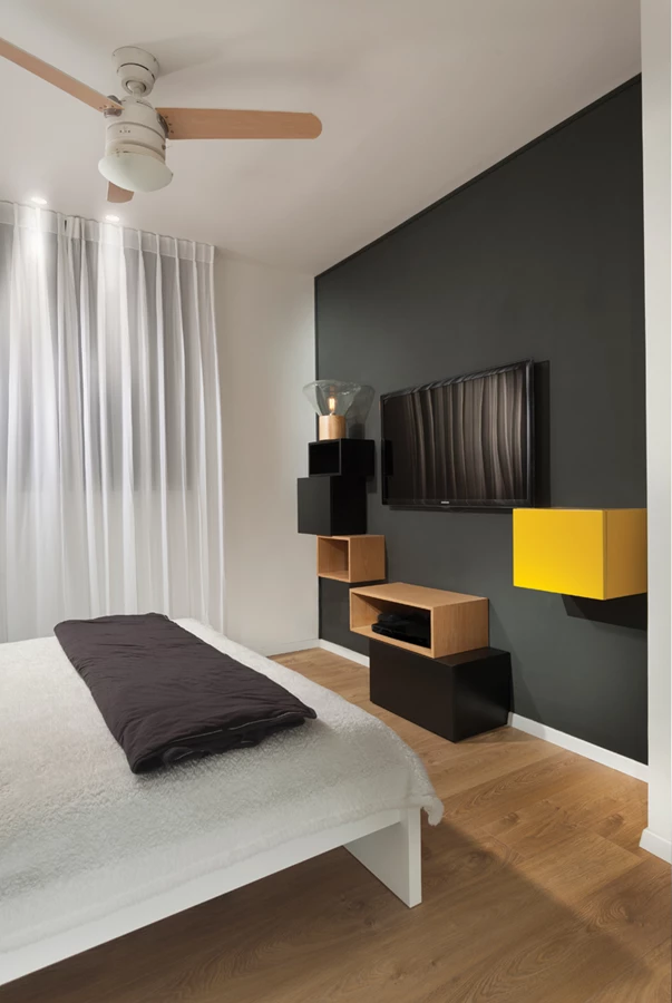 חדר השינה: ריצוף פרקט וקיר שחור כרקע לקוביות אחסון שבוצעו בעבודת נגרות.