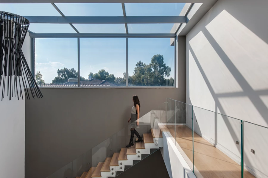 פתח האור בקיר ממשיך כקירוי חלקי שקוף של המעבר בקומה העליונה ושוטף אותו באור יום. פרקט אלון המשמש לריצוף הקומה מייצר רצף טבעי עם מדרכי העץ של גרם המדרגות המוביל אליה.