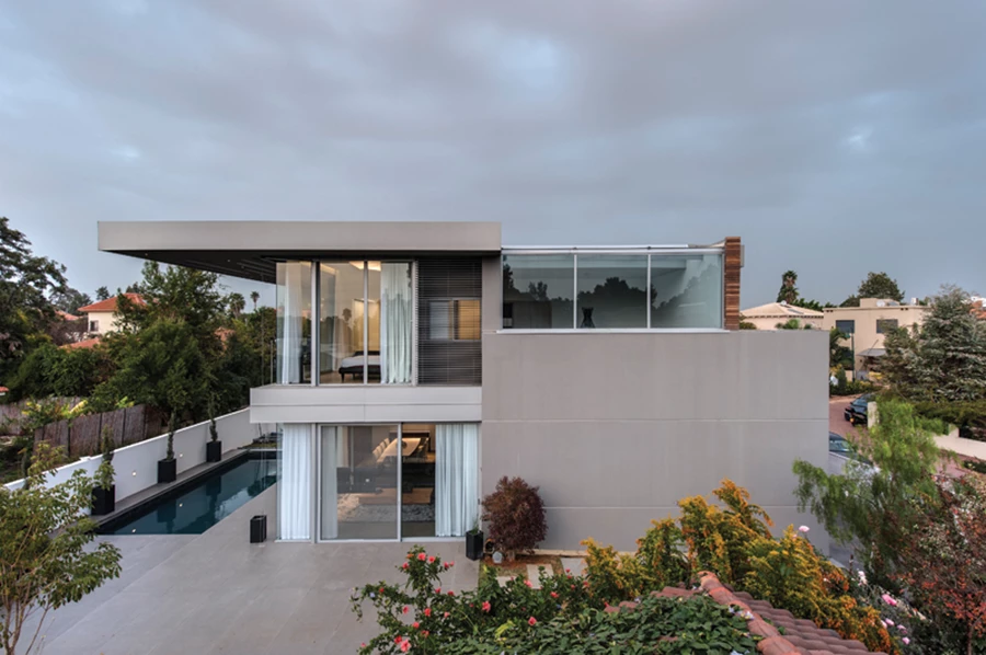 הבית במבט מהצד: מבנה נקי קווים, בריכה וגינה מטופחת .