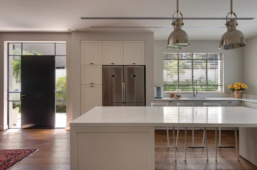 המטבח: חזיתות בעיצוב פאנלים חמים בגון שמנת וגימור צבע בתנור, ויחידת אי מרכזית מלווה בגופי תאורה גדולים עשויים מתכת במראה עכשווי. מטבח: