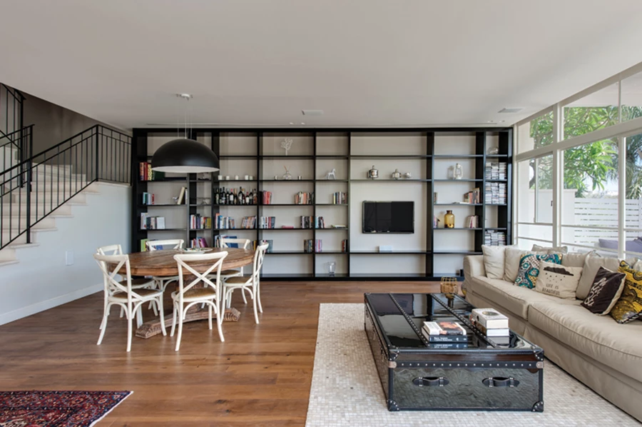 ספרייה שחורה בקווי עיצוב נקיים מכסה את פני שטחו של הקיר, ופינת האוכל משלבת שולחן עץ עם רגל מרכזית מאסיבית עם כיסאות בהירים במראה קליל יותר.