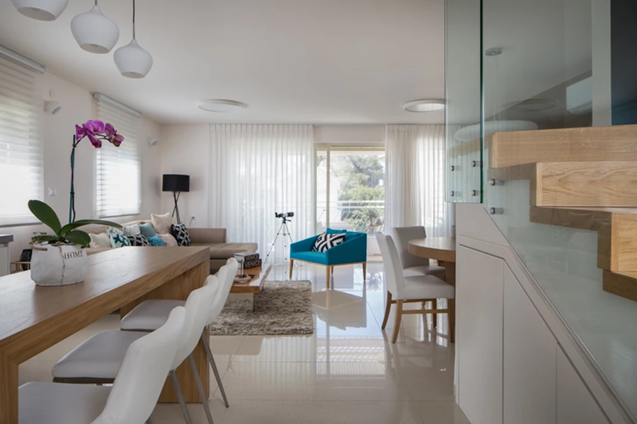 מחיצת זכוכית במקום קיר שהוסר פותחת את המבט מחלל המדרגות כלפי הסלון ומשווה יתר קלילות. החלל מתחת גרם המדרגות מנוצל לצרכי אחסון.