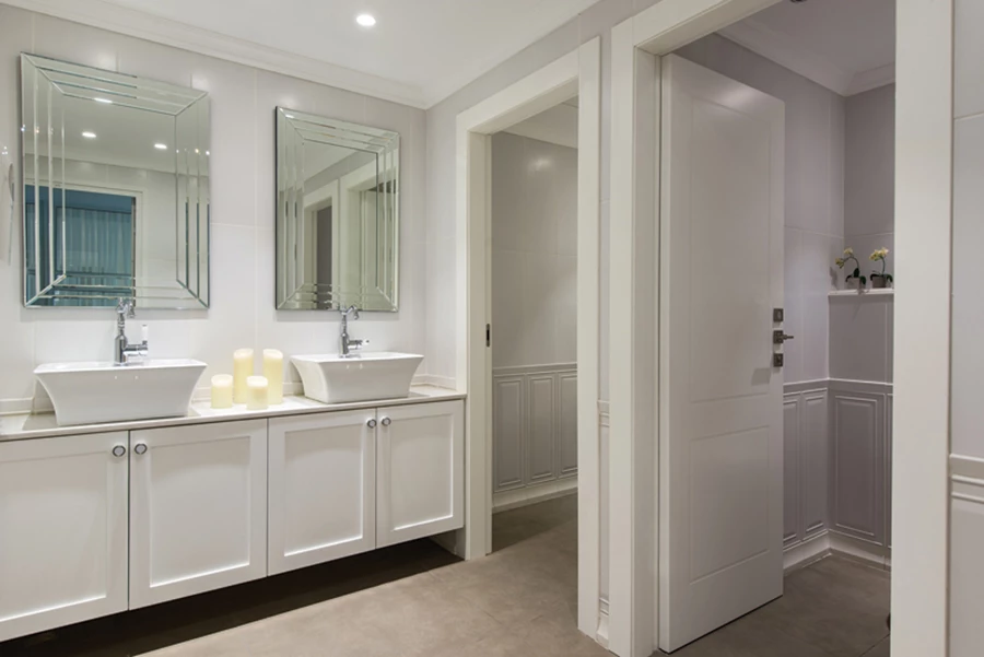 חלל השירותים בניחוח קלאסי: חזיתות פאנלים, משטח כיור מאבן קיסר דמוי שיש, כיור שולחני קלאסי ומראות מסוגננות.