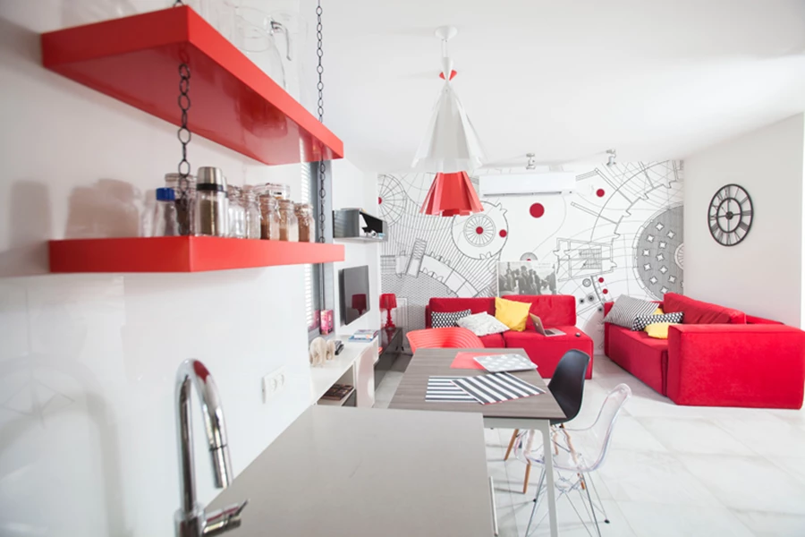 מבט מכיוון המטבח אל פינות האוכל והישיבה:  פינת ישיבה בריפוד אדום עז שהוזמנה ייעודית, כיסאות שונים זה מזה שמצטטים עיצובים איקוניים-מוכרים ו