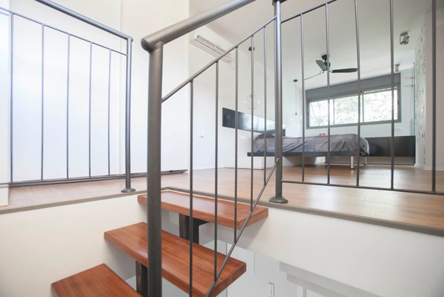 הקומה העליונה שהפכה למרחב אחד: ריצוף פרקט במבוק, ומחיצת זכוכית החוצצת בין אזורי השינה והרחצה. אזור הרחצה מרוצף ומחופה באבן צפחה ויחידת נגרות מרחפת מאזור השינה