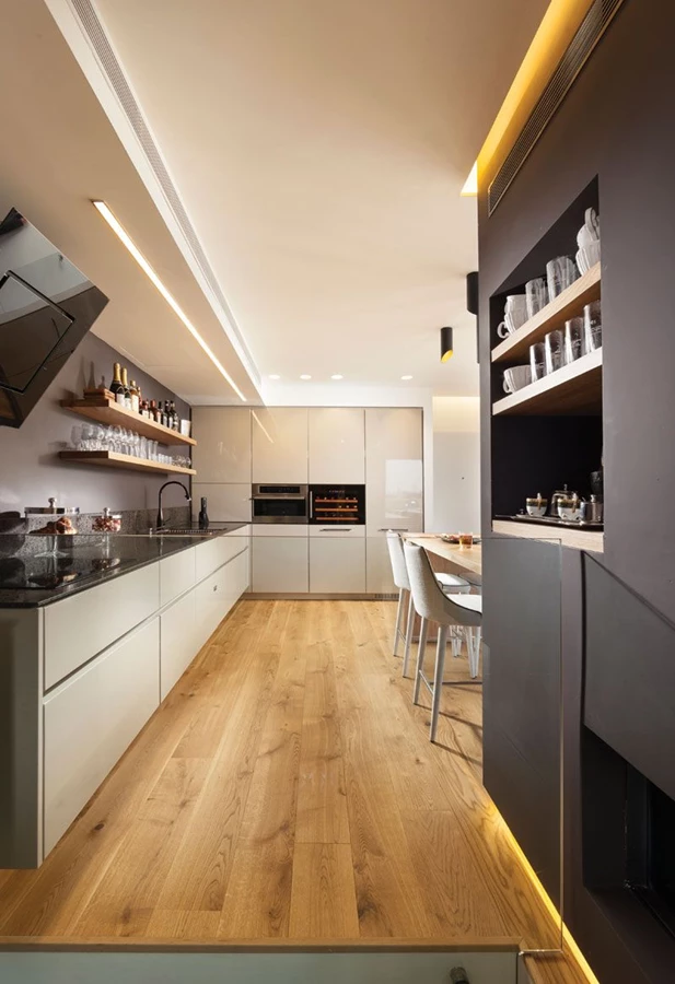 מבט מבעד מעקה הזכוכית השקוף של חלל המדרגות אל עבר המטבח: תאורה סמויה משתלבת מעל היחידה הבנויה ומתחתיה.