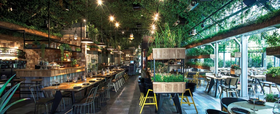 חלל החממה המרכזית: עתיר ירק שמשתלב על התקרה, הקירות ובינות לשולחנות. אריחי הריצוף בגון אפור ובגימור המדמה מראה רטוב ולח המאפיין רצפות בחממות. פריטי ריהוט וישיבה: