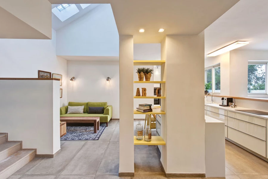 ניצול עמודים קונסטרוקטיביים שנותרו עם הסרת הקירות: מדפים צהובים שמשתלבים ביניהם מייצרים ספרייה כאלמנט חציצה אוורירי בין המבואה לבין כלל חלל המגורים.