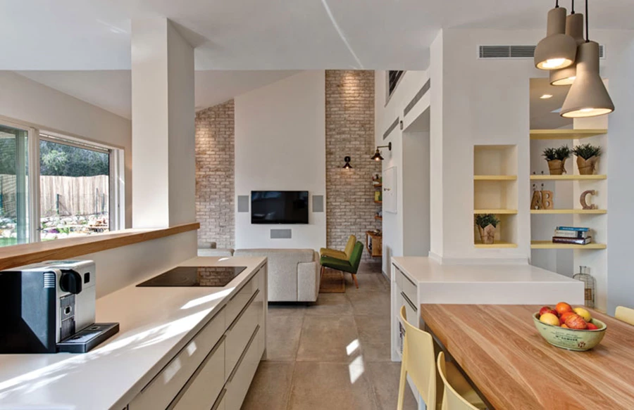 מבט מהמטבח אל אזור הסלון: קיר לבן עליו מותקן מסך הטלוויזיה משתלב בין קירות מחופי לבנים המדגישים את  ממד הגובה בחלק זה של החלל ומודגשים באמצעות תאורה שוטפת. פריטי ריהוט: