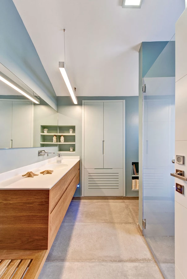 חדר הרחצה של יחידת ההורים: קירות בגון תכול מייצרים אווירת ספא רגועה, ובאזורים הרטובים משתלבים אריחי קרמיקה מדוקקים בגון לבן. אריחי חיפוי ואביזרים סניטאריים: