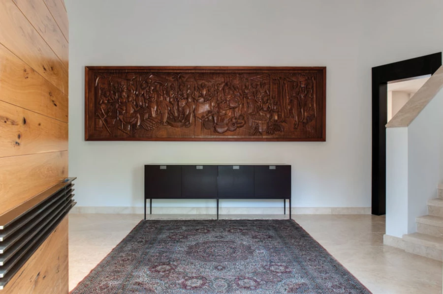 מבואת הכניסה: קונסולה שהותאמה לעבודת אמנות אהובה כבר מלמדת על שפת העיצוב. מימין נראה גרם המדרגות המוביל לקומה העליונה ומשמאל דלת הכניסה לחלל הסלון. ריצוף באבן טרוורטין. דלת כניסה ודלתות פנים: דלתות המושב