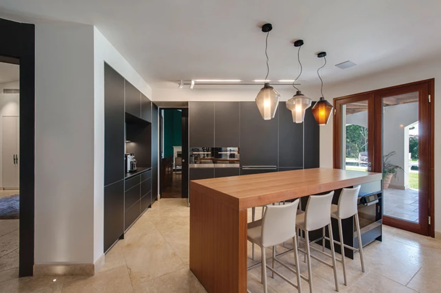 עיצוב שהותאם למתאר הגיאומטרי- מצולע של הקירות. יחידות קיר וכיור עם חזיתות אלומיניום בגון גרפיט, ודלפק ישיבה גבוה מעץ שהצבתו המתיישרת עם פתח היציאה לגן מתקבלת כאלכסונית ומלווה ב-3 גופי תאורה המלווים את מהלכו מלמעלה. בעומק התמונה, בהמשך לחלל המטבח, נראית פינת משפחה אינטימית. מטבח: בולטהאופ.