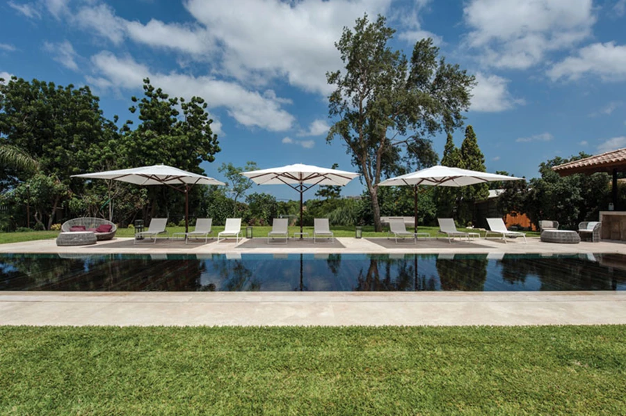 לאורך הבריכה: כורסאות שיזוף לבנות, שמשיות וריהוט גן המזמין התרווחות נינוחה