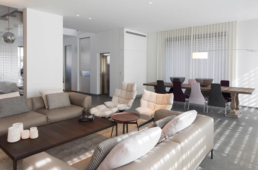 מבט למטבח שתוכנן תוך הגדרת אזור בישול ואזור אכילה: אזור הבישול מעוצב בקו מינימליסטי עם חזיתות גלוסי סטון לבנות, ובאזור האכילה משתלבים שולחן עץ עגול וכיסאות אדומים של אימס כנגיעת צבע המתכתבת עם כורסה פיסולית אדומה בעיצובו של KENNETH COPONBUE. גופי תאורה כסופים בעיצוב כדורי ומרקם מבריק משובצים במרחב הקומה כאלמנט מקשר היוצר עניין. מטבח: