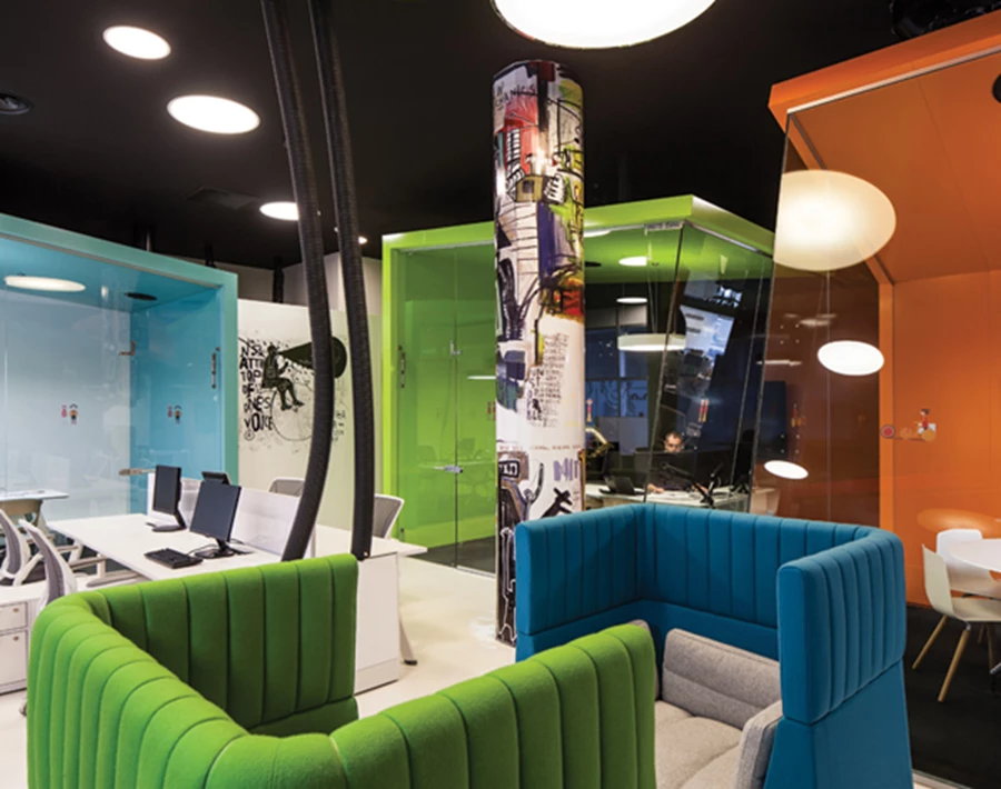 עמדת מנוחה אינטימית, עמוד מחופה מדבקות צבעוניות, ותשתיות שמשתלשלות מהתקרה נוכחות בחלל כחלק בלתי נפרד מהעיצוב.