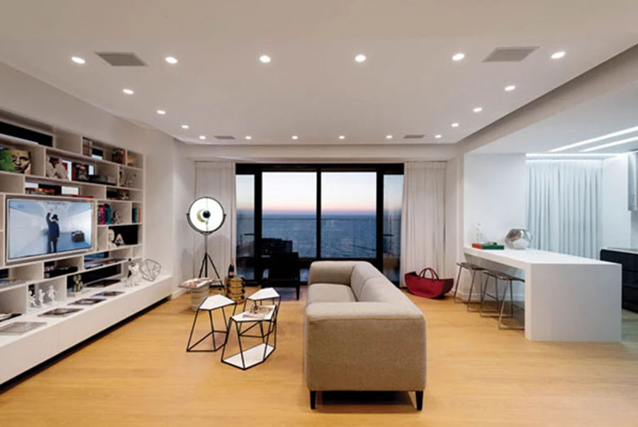 חלל המגורים והיציאה אל המרפסת. ריצוף בפרקט אלון, תקרה צפה משובצת גופי תאורה שקועים, ופריטי ריהוט בעיצוב נקי שנבחרו בקפידה או תוכננו ייעודית. שולחנות מצולעים, והדומים: קסטיאל, ספה וכורסת קש: קסטיאל As is.