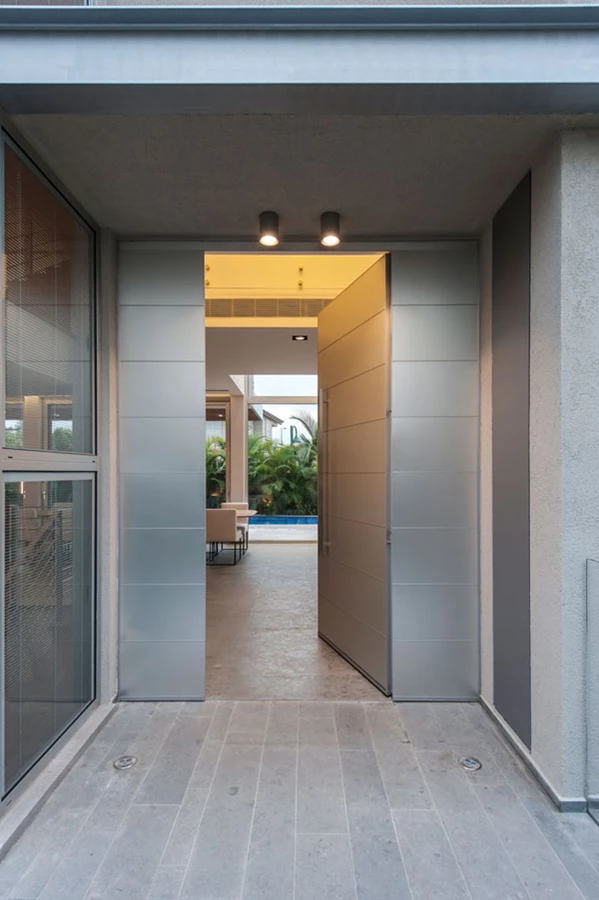 מבואת הכניסה החיצונית מחופה אלומיניום, וכך גם דלת הכניסה. משמאל נראית ויטרינה המעניקה הצצה ראשונית פנימה, ודרך הדלת הפתוחה נחשפת הגינה. דלת כניסה: 