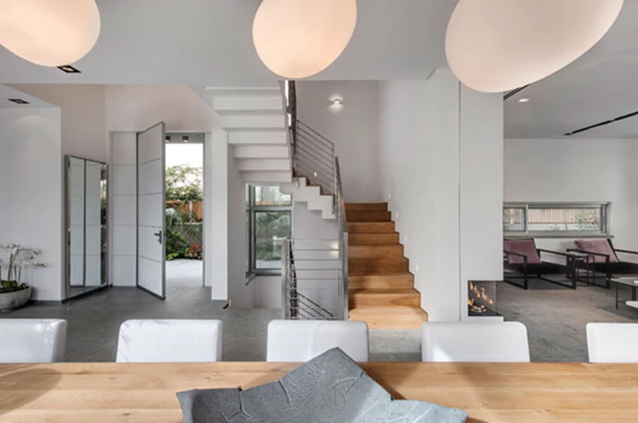 מבט מכיוון פינת האוכל אל עבר דלת הכניסה שמבחוץ מחופה באלומיניום ובחלל הפנים מופיעה בלבן. ריצוף באריחי אבן שייגריי בליטוש מט דמוי בטון, קירות לבנים ותאורה מבוססת על גופים שקועים. ריצוף: 