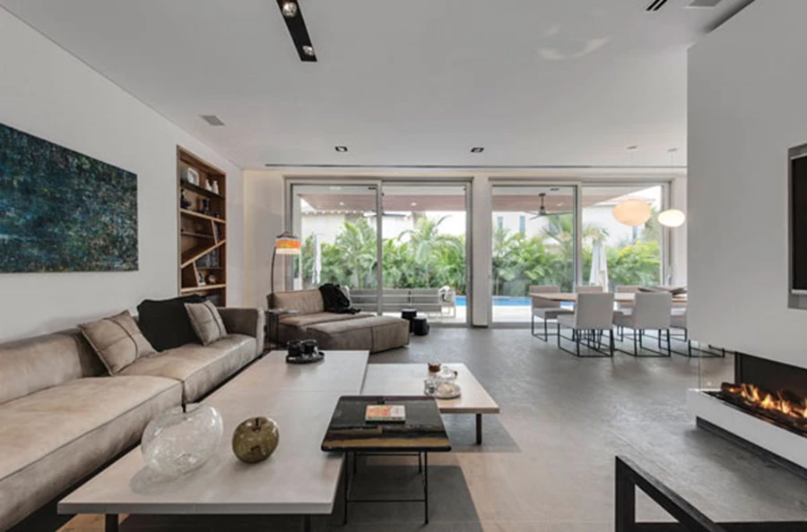 מבט מהסלון אל פינת האוכל והמטבח שבסוף ציר האורך, כמו גם אל מרחב החוץ.  העיצוב משלב פריטי ריהוט בקווים עכשוויים ונינוחים עם נגיעות עץ חמימות. ריהוט: HK חיים קרנדאג