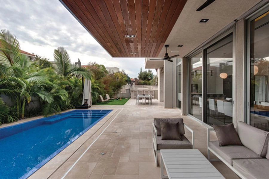 פרגולה המשלבת מסגרת אלומיניום ומילואת עץ, ופינות ישיבה ואוכל שהוצבו בחפיפה לפונקציות הפנים מייצרות נגישות נוחה ומידית בין שני המרחבים. בריכה: 