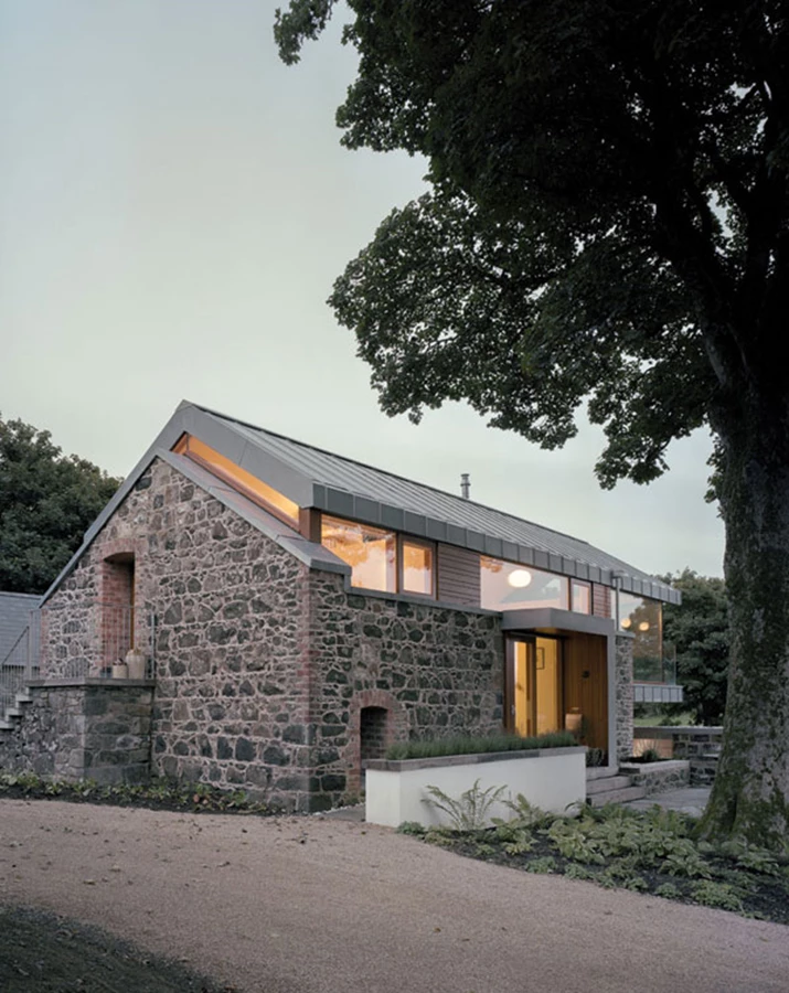 מבט מהכניסה לבית מדגיש את הגג המצופה מתכת הצף מעל קירות האבן.