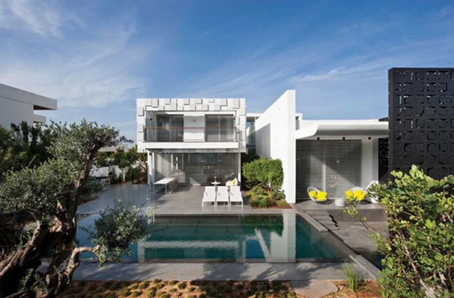 החזית האחורית: שני אגפי הבית והחצרות הפרטיות, מרחב מרוצף עם פינות ישיבה ואוכל, בריכה שאף היא מעוצבת ומחופה באבן בזלטינה ו