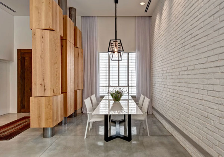 סמוך לכניסה, בין קיר לבנים צבוע לבן לבין אלמנט הקוביות: פינת האוכל תחומה כאזור אינטימי בחלל הפתוח.