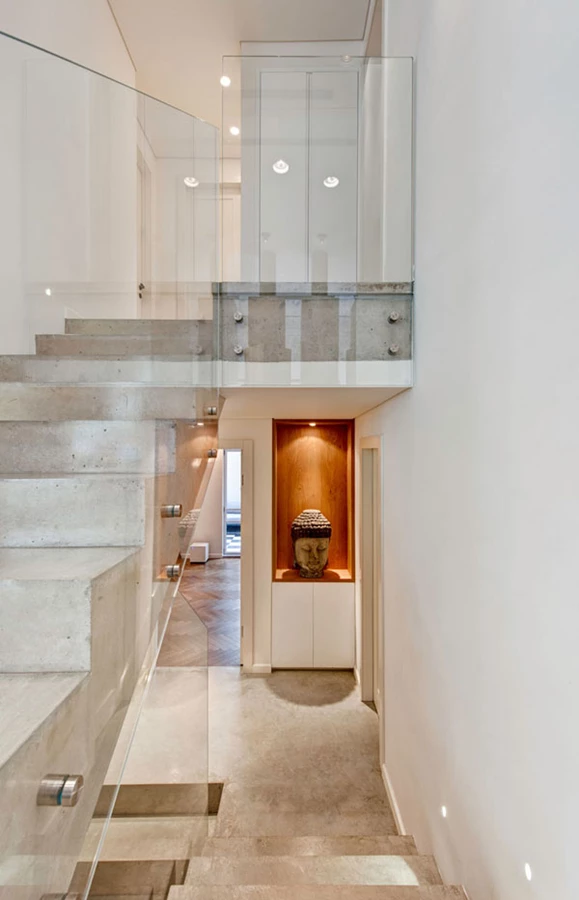 גרם המדרגות המקשר בין מפלסי החלל: מדרגות בטון ומעקה זכוכית שקוף.