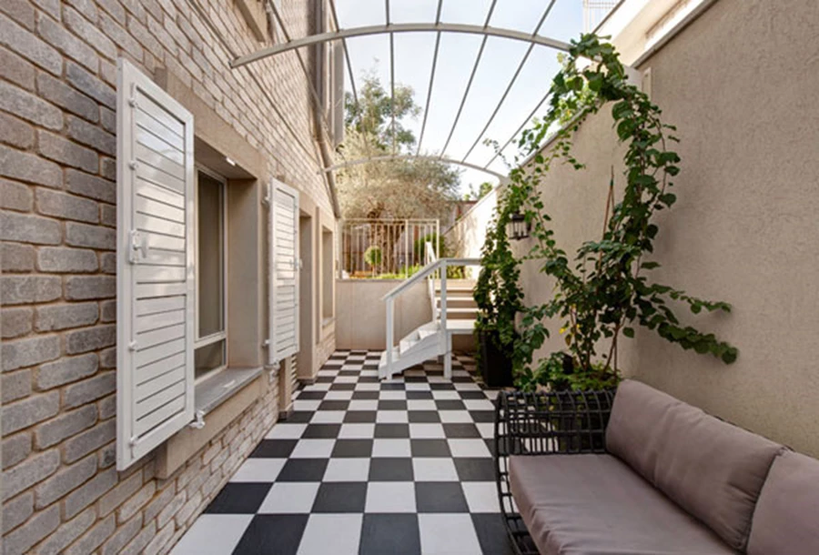 חצר אנגלית ביציאה מהחדר: ריצוף שחור-לבן כעין לוח שחמט, וחופת חוטי ברזל להשתרגות צמחים מצלה.