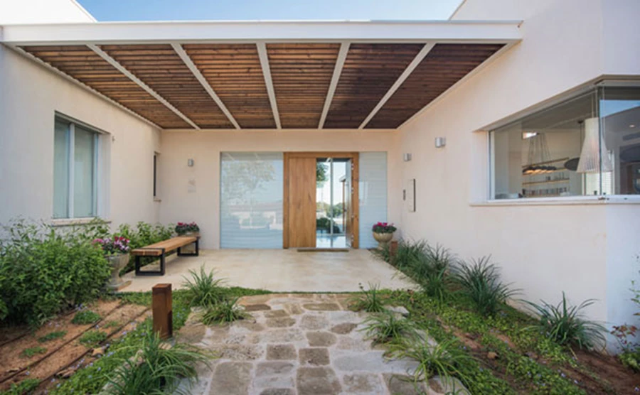 מבואה חיצונית בכניסה אל הבית. מראה טבעי ומזמין, קירוי בפרגולה המשלבת אלומיניום ועץ וספסל להתרגעות. גינון: